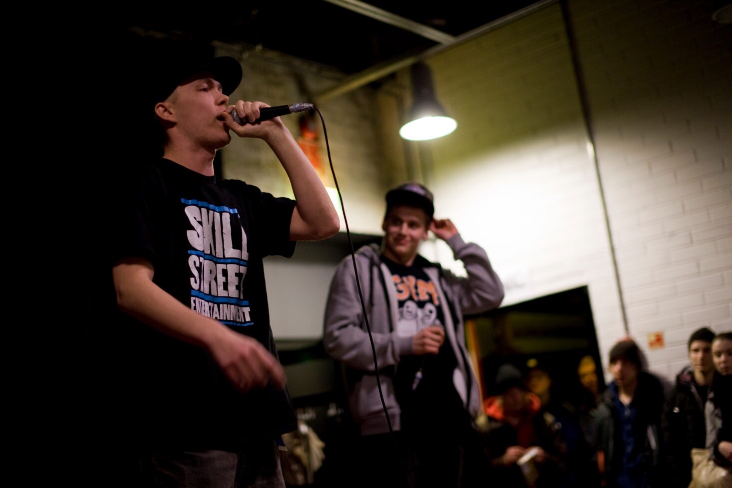 Rekami (vasemmalla) ja Gettomasa (oikealla) esiintyvät lavalla vuonna 2013, mikrofoni kädessä ja yleisö taustalla.